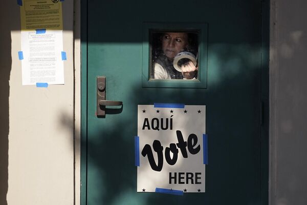 Una mujer con un rollo de pegatinas de "He votado" mira por la ventanilla de la puerta de un colegio electoral estadounidense en San Antonio. Una mujer con un rollo de pegatinas de "He votado" mira por la ventanilla de la puerta de un colegio electoral estadounidense en San Antonio. - Sputnik Mundo