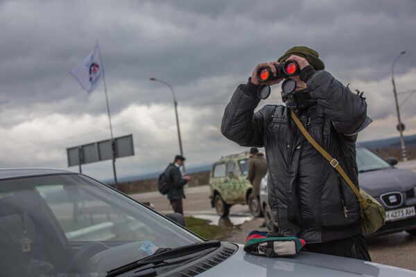 Además, el 28 de febrero comenzó la transición de las instalaciones estratégicas en el territorio de la península al control de las unidades de autodefensa. El primero en ser custodiado fue el aeropuerto internacional Simferópol, después - el aeropuerto Belbek cerca de Sebastopol. En la imagen: un residente local observa con prismáticos un puesto de control militar a la entrada del aeropuerto de Belbek. - Sputnik Mundo