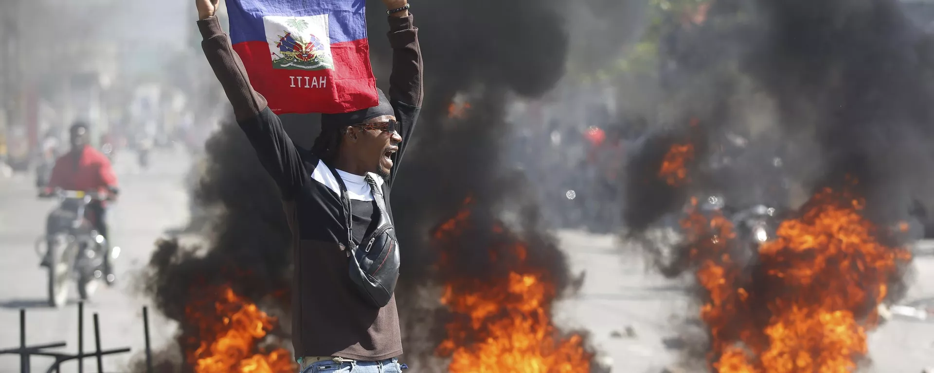 Un manifestante sostiene una bandera haitiana durante las protestas que exigen la dimisión del primer ministro Ariel Henry en Puerto Príncipe, Haití, el 1 de marzo de 2024 Un manifestante sostiene una bandera haitiana durante las protestas que exigen la dimisión del primer ministro Ariel Henry en Puerto Príncipe, Haití, el 1 de marzo de 2024 - Sputnik Mundo, 1920, 04.03.2024