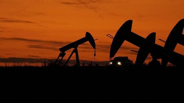 Un camión pasa junto a gatos de bombeo de petróleo al atardecer cerca de Karnes City, Texas, el 1 de noviembre de 2023. - Sputnik Mundo