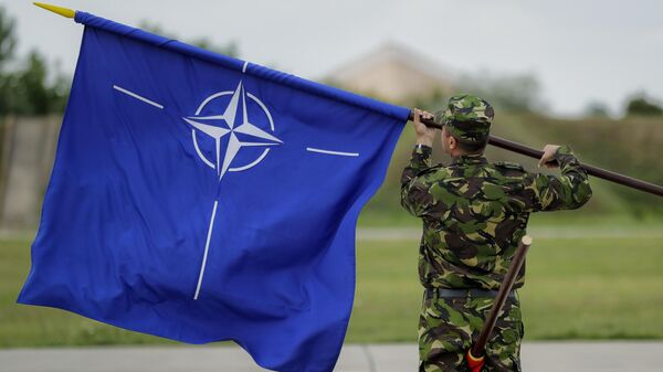 Un militar rumano enarbola la bandera de la OTAN tras la visita del ministro de Defensa británico, Michael Fallon, a una base aérea en Rumanía, el 14 de junio de 2017  - Sputnik Mundo