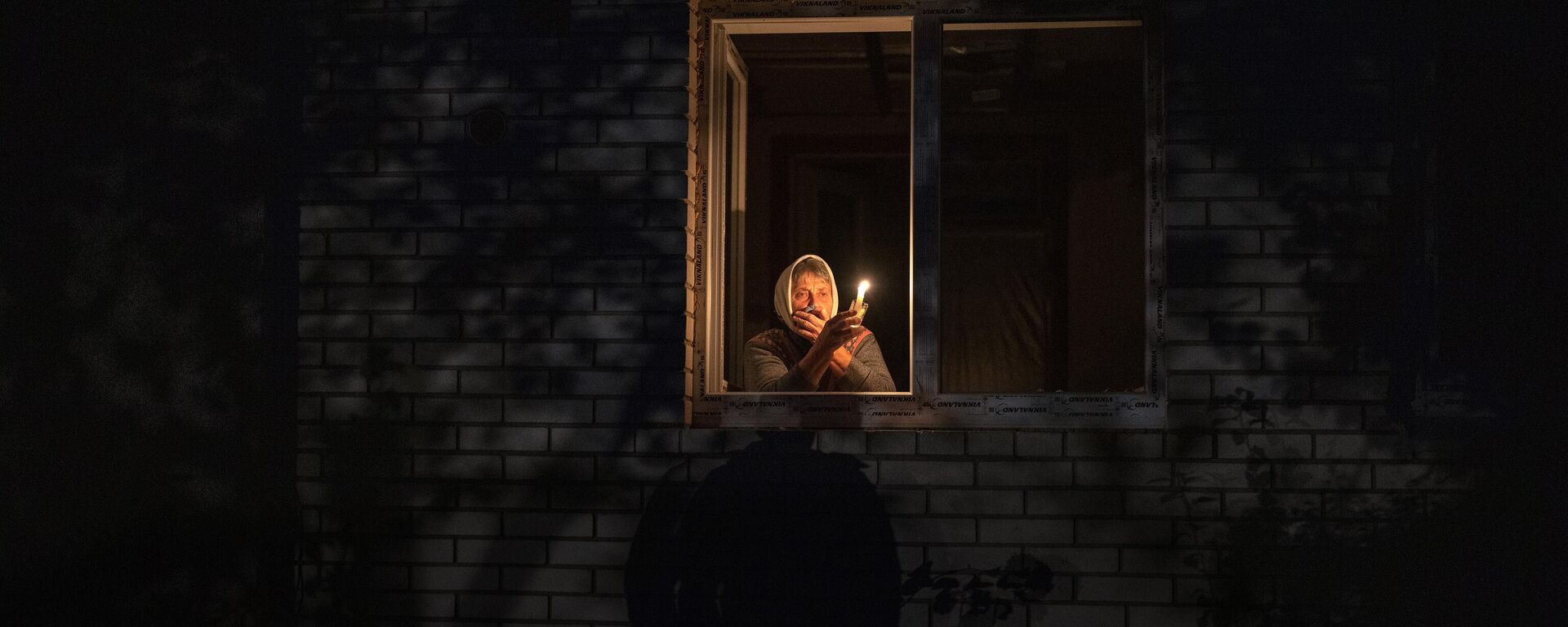 Mujer mira por la ventana mientras sostiene una vela para la luz dentro de su casa durante un corte de energía, en Borodianka, región de Kiev, Ucrania, el 20 de octubre de 2022. - Sputnik Mundo, 1920, 21.04.2024