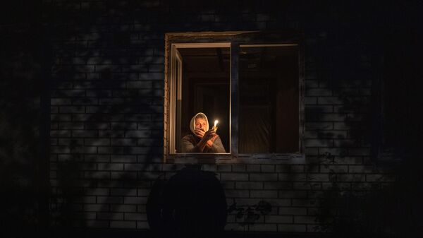 Mujer mira por la ventana mientras sostiene una vela para la luz dentro de su casa durante un corte de energía, en Borodianka, región de Kiev, Ucrania, el 20 de octubre de 2022. - Sputnik Mundo
