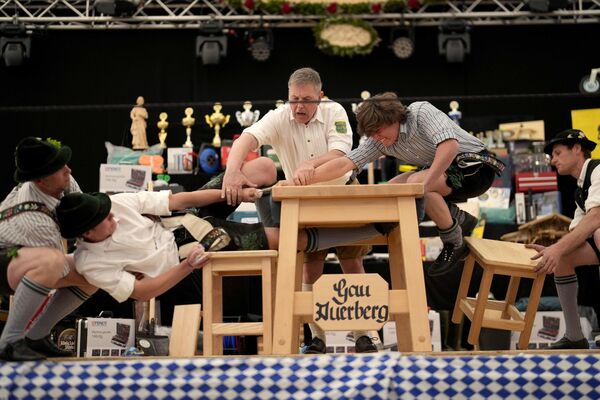 Hombres vestidos con trajes tradicionales intentando arrastrar al oponente por encima de la mesa en el campeonato alemán de Fingerhakeln o lucha con los dedos, en Bernbeuren. Los competidores se disputan el título en este deporte rural tradicional en el que el ganador tiene que tirar de su oponente por encima de una línea marcada en la mesa. - Sputnik Mundo