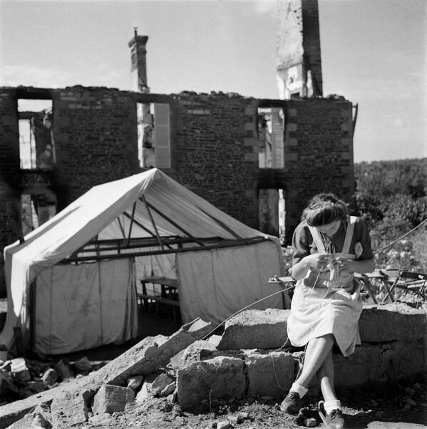 En la mañana del 7 de junio de 1944, unos 3.000 civiles de Normandía ya habían perecido bajo las bombas aliadas.En la foto: una mujer teje cerca de una tienda para refugiados, entre las ruinas de Mortain, Normandía. - Sputnik Mundo