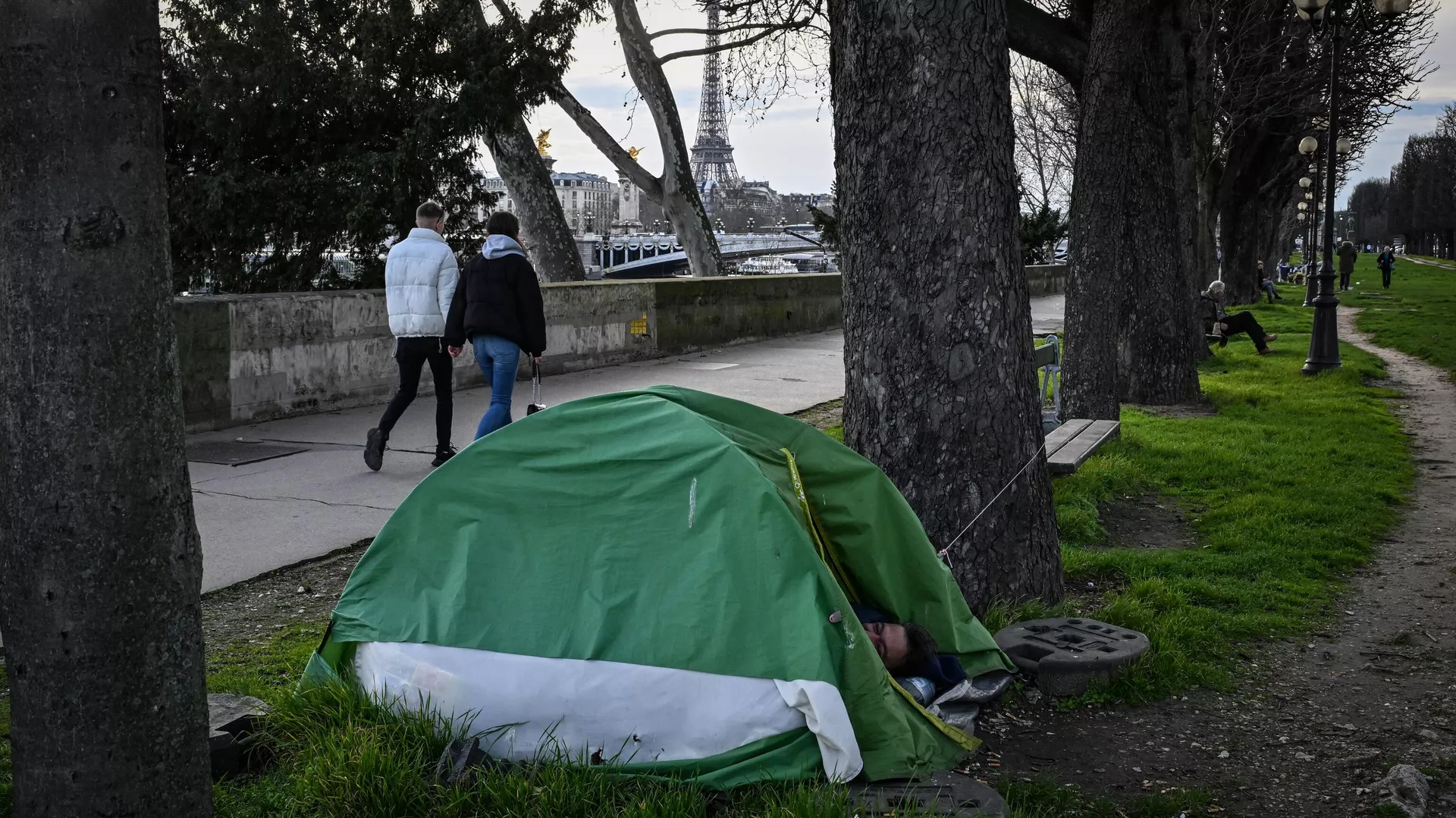 Un indigente duerme en su tienda mientras los peatones caminan cerca del río Sena con la Torre Eiffel al fondo en el centro de París Un indigente duerme en su tienda mientras los peatones caminan cerca del río Sena con la Torre Eiffel al fondo en el centro de París