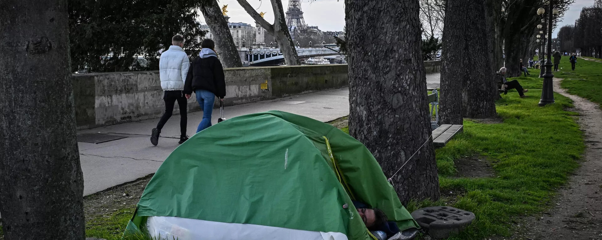 Un indigente duerme en su tienda mientras los peatones caminan cerca del río Sena con la Torre Eiffel al fondo en el centro de París Un indigente duerme en su tienda mientras los peatones caminan cerca del río Sena con la Torre Eiffel al fondo en el centro de París - Sputnik Mundo, 1920, 06.06.2024