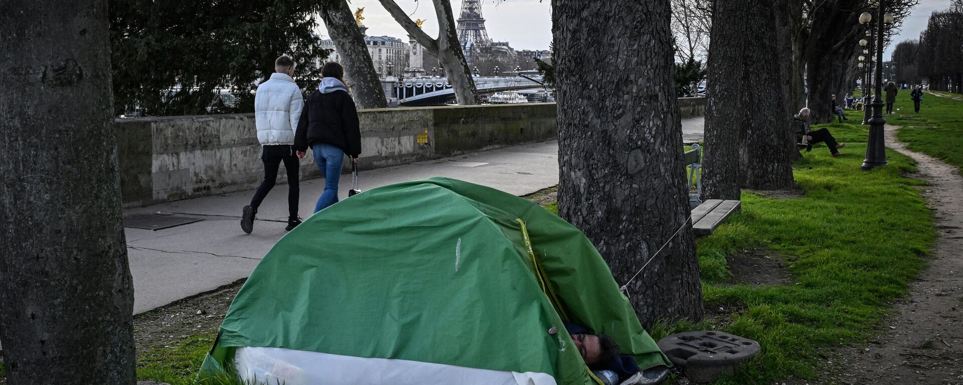 Un indigente duerme en su tienda mientras los peatones caminan cerca del río Sena con la Torre Eiffel al fondo en el centro de París - Sputnik Mundo, 1920, 06.06.2024