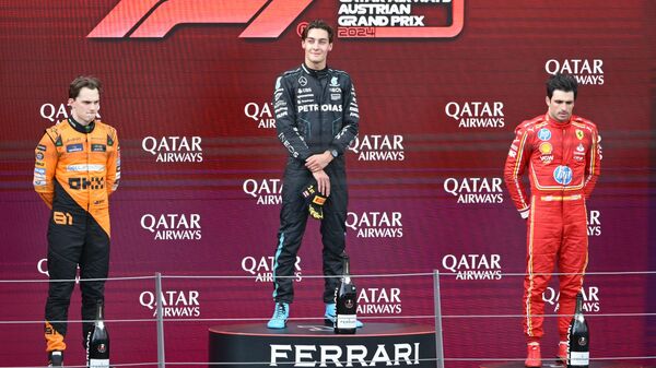 El piloto australiano de McLaren Oscar Piastri, segundo clasificado, el británico de Mercedes George Russell, ganador, y el español de Ferrari Carlos Sainz, tercero, reaccionan en el podio tras el Gran Premio de Austria de Fórmula 1, el 30 de junio de 2024 - Sputnik Mundo