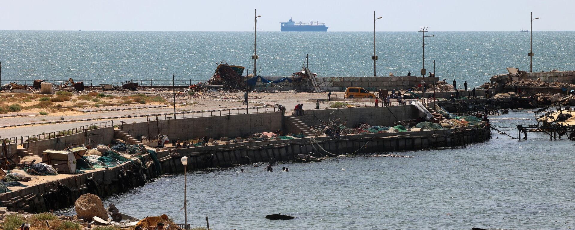 Palestinos caminan junto a un embarcadero en la ciudad de Gaza con vistas a los buques de la Armada frente a la costa como parte de un corredor marítimo humanitario anunciado por el Mando Central de Estados Unidos (CENTCOM) en mayo de 2024.  - Sputnik Mundo, 1920, 01.07.2024