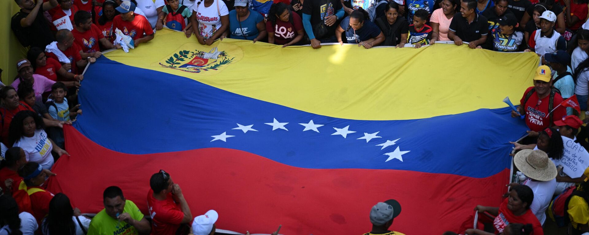 Una bandera venezolana sostenida entre simpatizantes del presidente y candidato presidencial de Venezuela, Nicolás Maduro - Sputnik Mundo, 1920, 28.07.2024