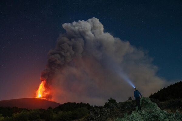 Una persona observando las nubes y la lava sobre el volcán Etna durante una erupción en la isla  italiana de Sicilia. - Sputnik Mundo