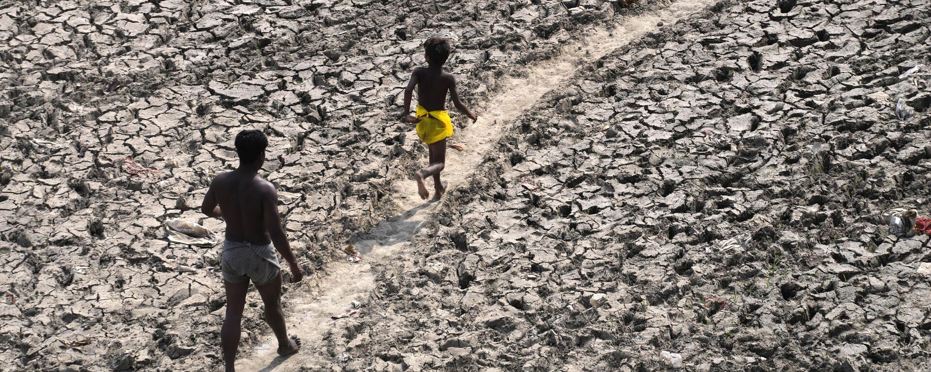 Un hombre y un niño caminan por el lecho casi seco de un río tras las altas temperaturas, la India. - Sputnik Mundo, 1920, 30.07.2024