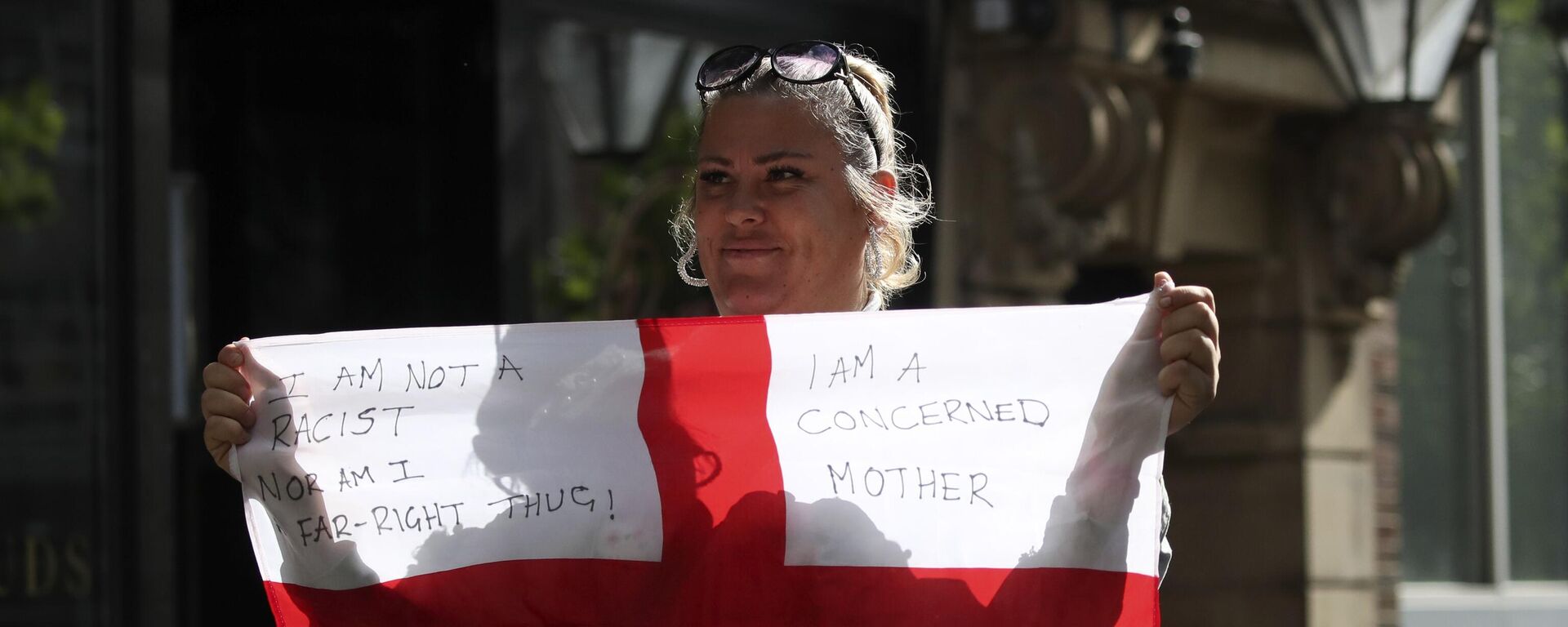 Una mujer sostiene una bandera británica con lemas contra la inmigración durante una protesta que desató la violencia - Sputnik Mundo, 1920, 15.08.2024