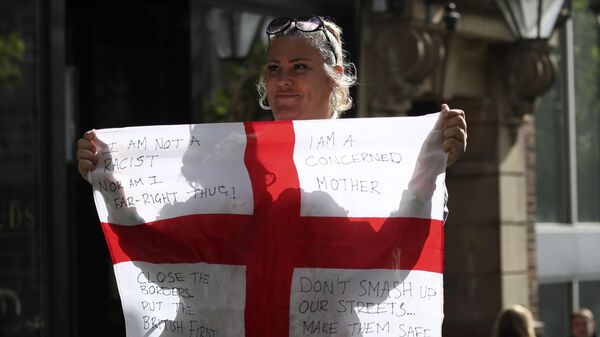 Una mujer sostiene una bandera británica con lemas contra la inmigración durante una protesta que desató la violencia - Sputnik Mundo