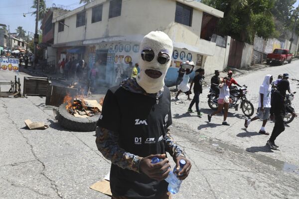 Un manifestante enmascarado pasando junto a una barricada en llamas instalada por protestantes que exigen a la Policía y a las autoridades que tomen medidas inmediatas contra las bandas en la ciudad de Puerto Príncipe, Haití. - Sputnik Mundo