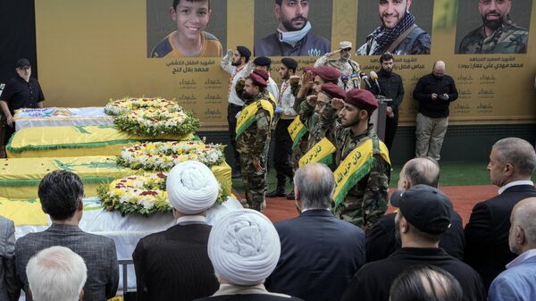 Combatientes de Hizbulá saludan junto a los ataúdes de cuatro víctimas que murieron el martes después de que explotaran sus buscapersonas portátiles, en el suburbio sur de Beirut, Líbano, el miércoles 18 de septiembre de 2024.  - Sputnik Mundo