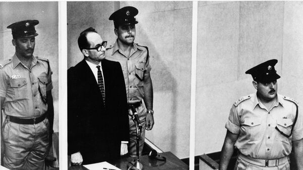 Adolf Eichmann de pie en su jaula de cristal, flanqueado por guardias, en la sala del tribunal de Jerusalén donde fue juzgado en 1961 por crímenes de guerra cometidos durante la Segunda Guerra Mundial.  - Sputnik Mundo