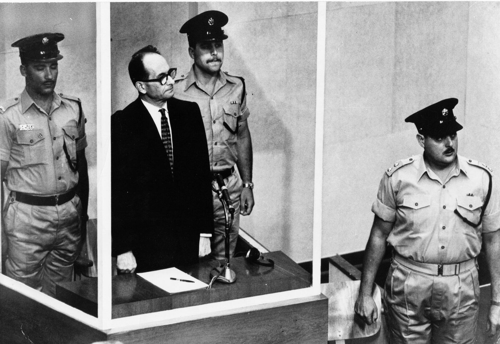 Adolf Eichmann de pie en su jaula de cristal, flanqueado por guardias, en la sala del tribunal de Jerusalén donde fue juzgado en 1961 por crímenes de guerra cometidos durante la Segunda Guerra Mundial.  - Sputnik Mundo, 1920, 21.09.2024