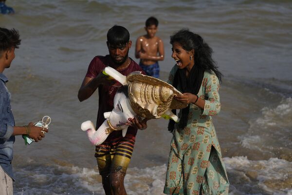 Fieles reaccionan mientras sostienen la cabeza de un ídolo del dios hindú Ganesha con cabeza de elefante en la bahía de Bengala, el último día del festival Ganesh Chaturthi en Chennai, la India. - Sputnik Mundo