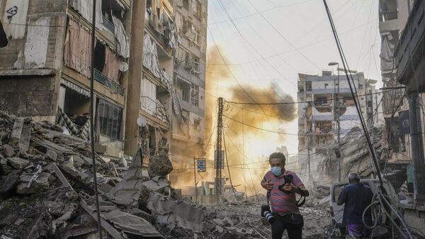 Un fotógrafo corre para cubrirse mientras se levanta humo en el fondo después de un ataque aéreo israelí en Dahiyeh, Beirut, Líbano, el viernes 4 de octubre de 2024. (Foto AP/Hassan Ammar) - Sputnik Mundo