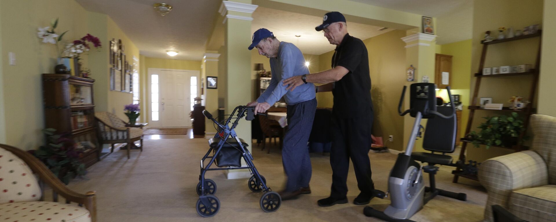 El cuidador Warren Manchess, a la derecha, cruza la sala con Paul Gregoline, de 92 años, en Noblesville, Indiana. Tres días a la semana, Manchess, de 74 años, llega a la casa de Gregoline y le da a la esposa del electricista jubilado un descanso necesario. La creciente demanda de servicios para personas mayores, como asistentes de atención médica domiciliaria, está siendo satisfecha por un segmento sorprendente de la fuerza laboral: otras personas mayores. (Archivo).  - Sputnik Mundo, 1920, 07.10.2024