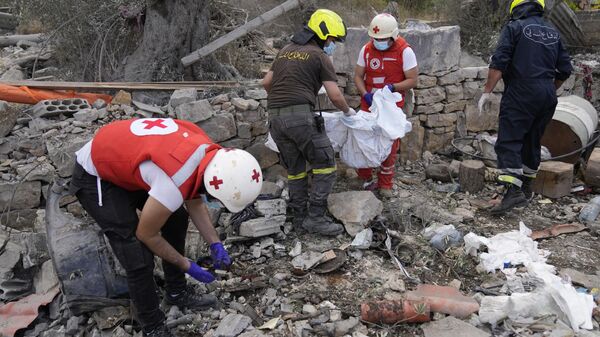 Voluntarios de la Cruz Roja Libanesa y trabajadores de la Defensa Civil retiran los restos de personas asesinadas de los escombros de un edificio destruido en el lugar del ataque aéreo israelí del lunes en la aldea de Aito, al norte del Líbano, el martes 15 de octubre de 2024. (Foto AP/Hussein Malla) - Sputnik Mundo