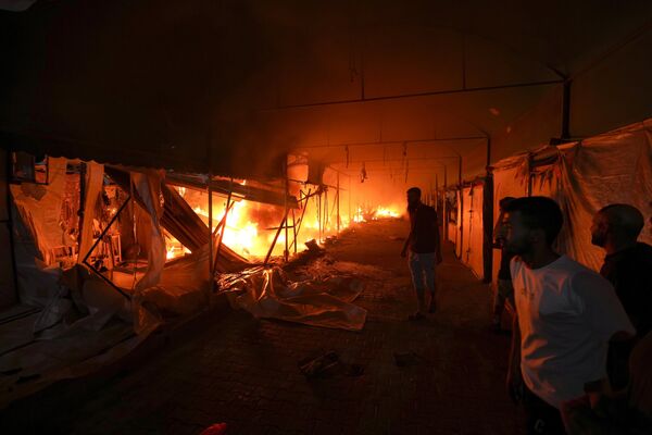 Un grupo de palestinos observa un incendio tras un ataque israelí contra el patio de un hospital en la Franja de Gaza. - Sputnik Mundo