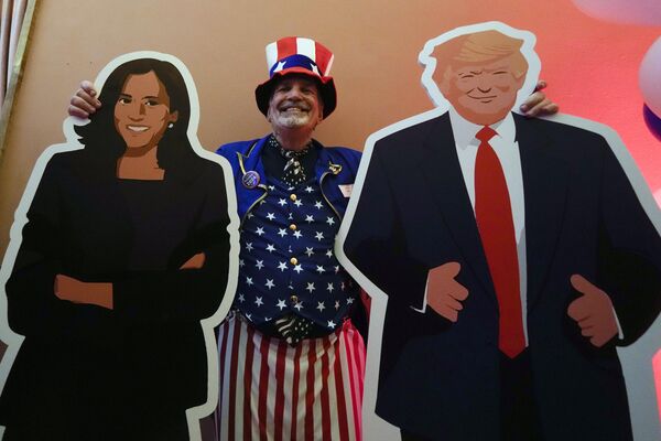 El funcionario del Consulado de EEUU Timothy Lockwood posa con carteles de Kamala Harris y Donald Trump durante la noche electoral en Milán, Italia. - Sputnik Mundo