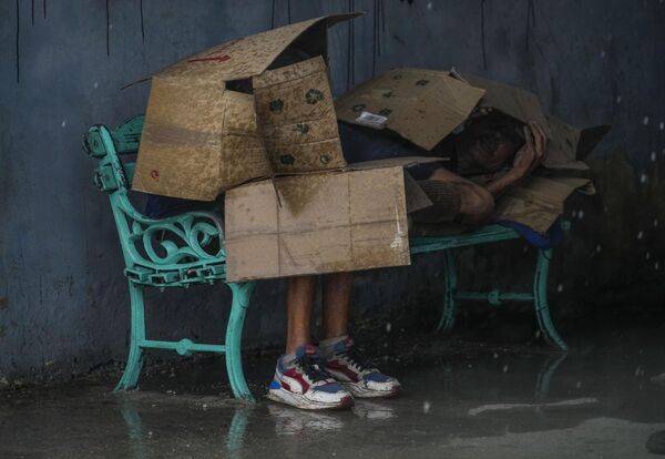 Un grupo de personas en una parada de autobús se cubre con cartones para protegerse del viento y la lluvia durante el huracán Rafael en La Habana,  capital de Cuba. - Sputnik Mundo