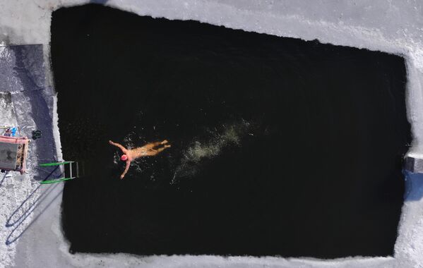 Un nadador de invierno se desplaza en una piscina excavada en un lago helado junto al río Songhua en Harbin, en la provincia china de Heilongjiang. - Sputnik Mundo