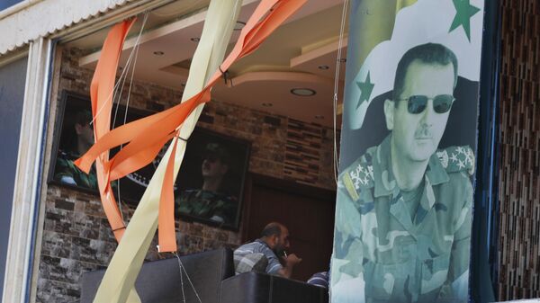 Un cartel con la imagen del expresidente sirio Bashar Asad en una ventana dañada por la explosión - Sputnik Mundo