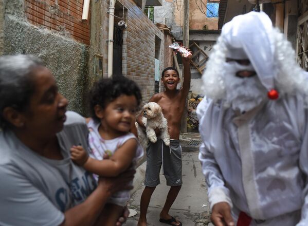 Una persona disfrazada de Papá Noel visita la favela de Mare para dar caramelos y regalos a los niños en la ciudad brasileña de Río de Janeiro. - Sputnik Mundo