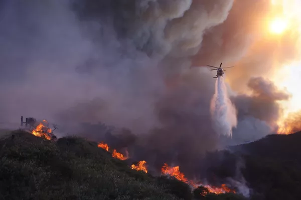 Un helicóptero lanza agua sobre el avance del incendio en Pacific Palisades. - Sputnik Mundo