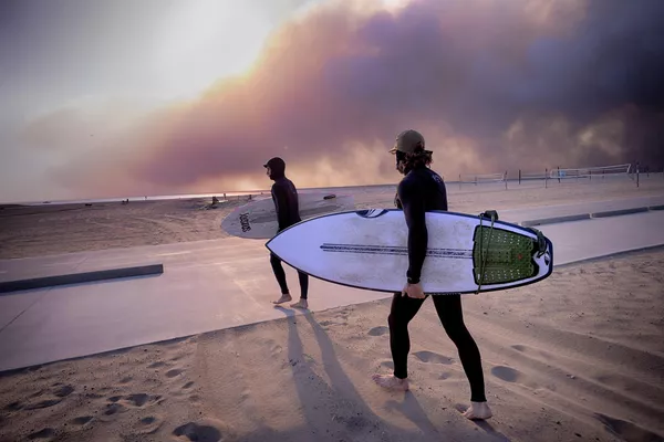 Los surfistas Shaun Rosenberg y Teal Greene se lanzan a las olas bajo un cielo ennegrecido por un incendio forestal en Pacific Palisades, durante la puesta de sol en Santa Mónica, California. - Sputnik Mundo