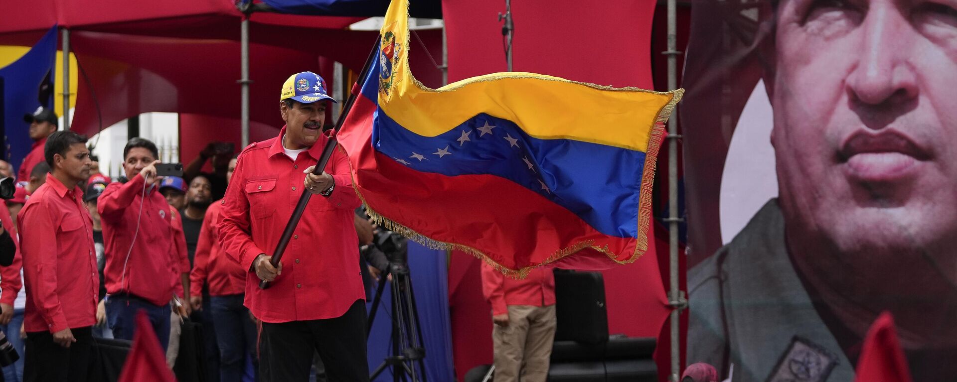 El presidente Nicolás Maduro ondea una bandera de Venezuela adelante del retrato de Hugo Chávez - Sputnik Mundo, 1920, 15.04.2025