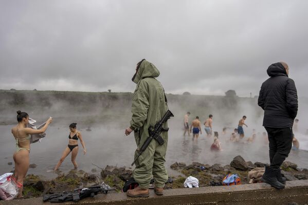 Un soldado israelí monta guardia mientras varias personas se bañan en el agua caliente de un manantial subterráneo. - Sputnik Mundo