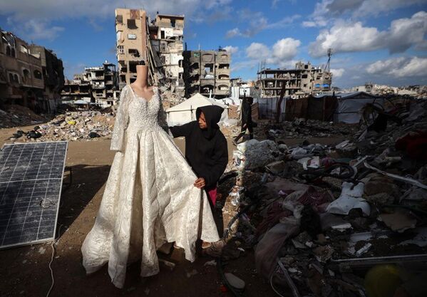 El propietario de una tienda palestina, destruida por los ataques israelíes, muestra vestidos de novia a la venta en maniquíes. - Sputnik Mundo