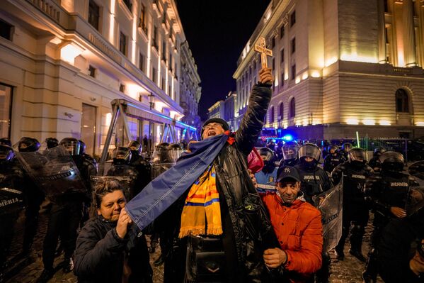 Una mujer grita sosteniendo una cruz frente a policías que bloquean una calle tras los enfrentamientos con partidarios de Calin Georgescu después de que el órgano electoral de Rumanía rechazara su candidatura en la repetición de las elecciones presidenciales en Bucarest, Rumanía. - Sputnik Mundo