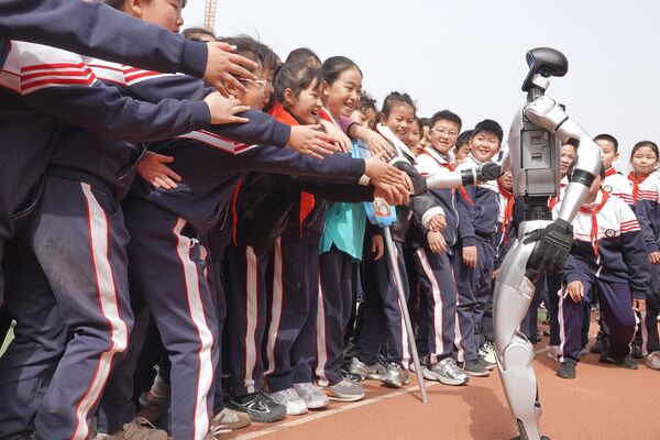 Unos estudiantes hacen cola para estrechar la mano de un robot humanoide Unitree G1, en una escuela primaria en Yantai, provincia china de Shandong. Unos estudiantes hacen cola para estrechar la mano de un robot humanoide Unitree G1, en una escuela primaria en Yantai, provincia china de Shandong. - Sputnik Mundo