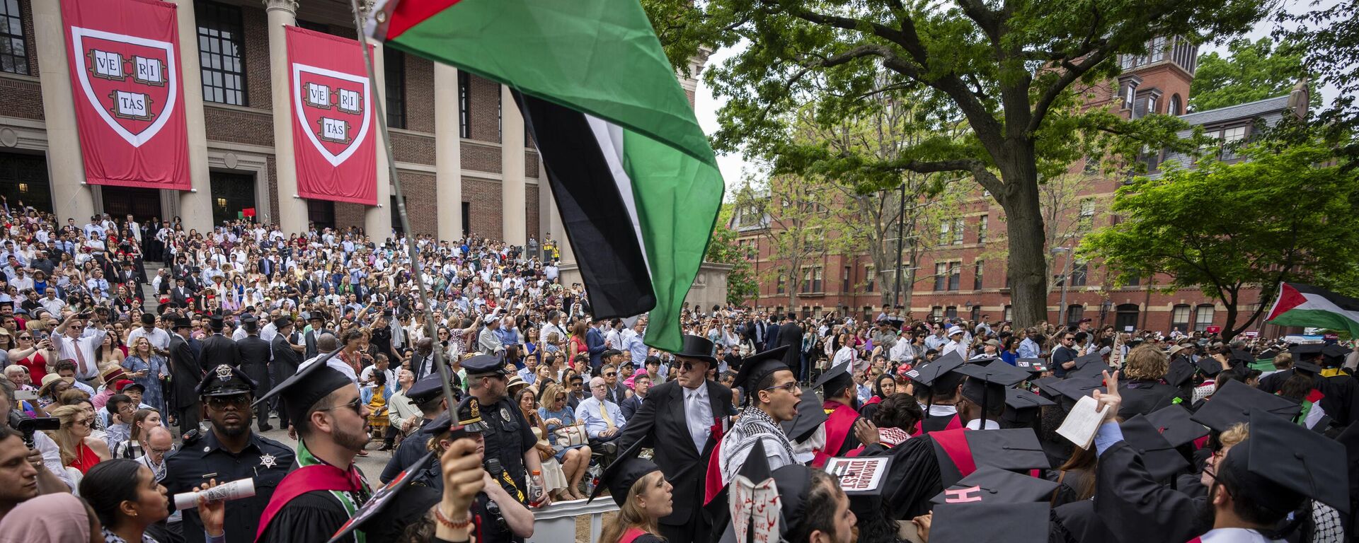 Estudiantes que se gradúan sostienen banderas palestinas y corean mientras protestan por los 13 estudiantes a los que se les ha prohibido graduarse debido a sus manifestaciones en la Universidad Harvard. - Sputnik Mundo, 1920, 23.04.2025