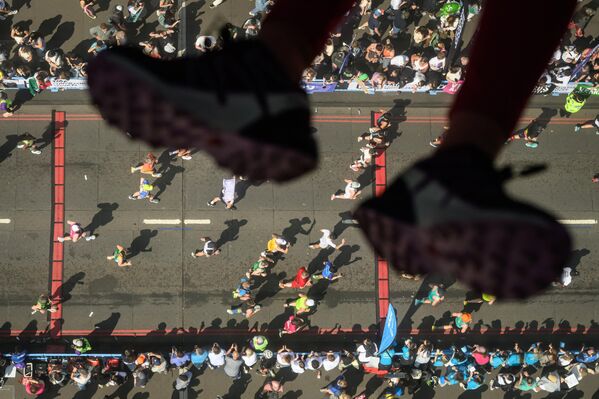 Se ven las piernas de un niño sentado en un panel de vidrio, mirando a los corredores que cruzan el Tower Bridge durante el Maratón de Londres, en Reino Unido. El Maratón de Londres fue fundado por los atletas Chris Brasher y John Disley en 1981 y se desarrolla en un recorrido plano alrededor del río Támesis, comenzando en Blackheath y finalizando en The Mall. - Sputnik Mundo