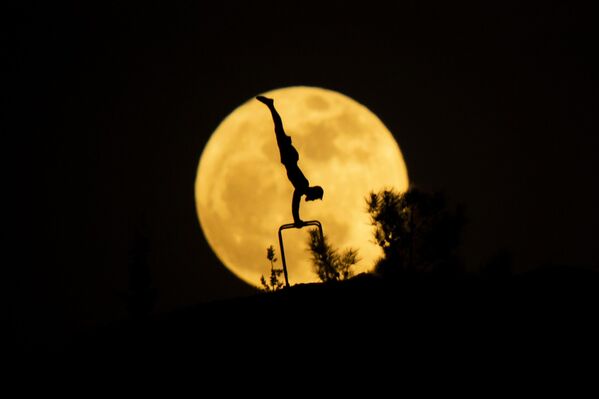 La luna llena se ve detrás de la silueta de un hombre haciendo gimnasia en la capital de la Región Autónoma Kurda, Erbil. - Sputnik Mundo
