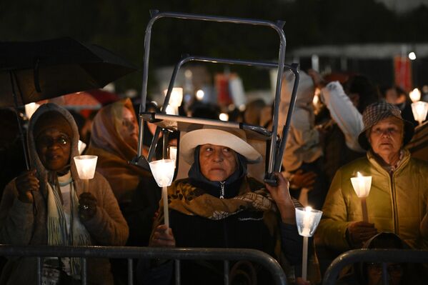 Una peregrina con una vela en la mano se protege con un taburete invertido bajo la lluvia mientras las personas abarrotan el Santuario de Fátima antes de la procesión,  Fátima, Portugal. - Sputnik Mundo