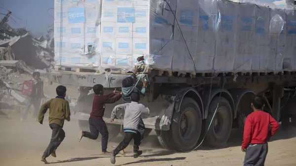 Palestinos persiguen camiones de ayuda humanitaria que llegaron a través del paso fronterizo de Kerem Shalom desde Egipto a la Franja de Gaza, en Rafah, el 21 de enero de 2025 - Sputnik Mundo