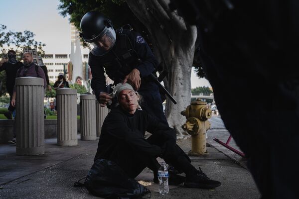 Un agente de la Policía ayuda a una manifestante atropellada por un caballo de los servicios policiales durante los enfrentamientos con las fuerzas del orden en Los Ángeles. - Sputnik Mundo