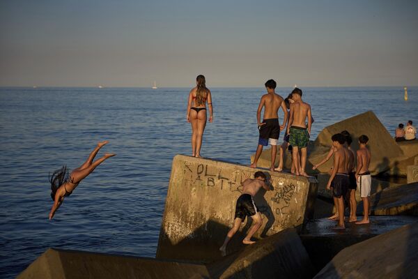Jóvenes nadadores saltan al agua desde una roca en un rompeolas, en un día caluroso en Barcelona, España. Jóvenes nadadores saltan al agua desde una roca en un rompeolas, en un día caluroso en Barcelona, España. - Sputnik Mundo