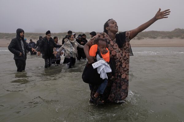 Una mujer con un niño en brazos ruega a los traficantes que la dejen subir a un pequeño bote, que se acerca a la costa para recoger a más personas en medio de una espesa niebla en la localidad de Gravelines, Francia.El barco llegó a través de la niebla, ya lleno de migrantes que habían abordado más al norte de la costa, con la esperanza de que algunos más pudieran entrar. Una mujer con un niño en brazos ruega a los traficantes que la dejen subir a un pequeño bote, que se acerca a la costa para recoger a más personas en medio de una espesa niebla en la localidad de Gravelines, Francia.El barco llegó a través de la niebla, ya lleno de migrantes que habían abordado más al norte de la costa, con la esperanza de que algunos más pudieran entrar. - Sputnik Mundo