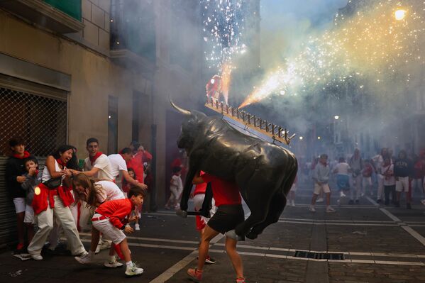 Menores y adultos se ven perseguidos por el Toro de Fuego, mientras corre por las calles durante los encierros de San Fermín, el 7 de julio de 2025 en Pamplona, España. Durante los sanfermines, cada mañana, una multitud de personas corren con seis toros y seis novillos por un recorrido serpenteante a través de estrechas calles, hasta la plaza de toros de la ciudad. Más tarde, esa misma noche, se da muerte a los animales en una corrida nocturna, una tradición que se remonta a la época medieval. La fiesta, de una semana de duración, también incluye fuegos artificiales, procesiones religiosas, bailes folclóricos, conciertos y bebida a todas horas. - Sputnik Mundo