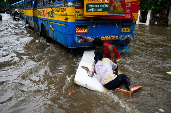 Menores flotan en una balsa improvisada de lámina de espuma de polietileno en una calle anegada tras las fuertes lluvias de la noche anterior, en la ciudad india de Calcuta. - Sputnik Mundo